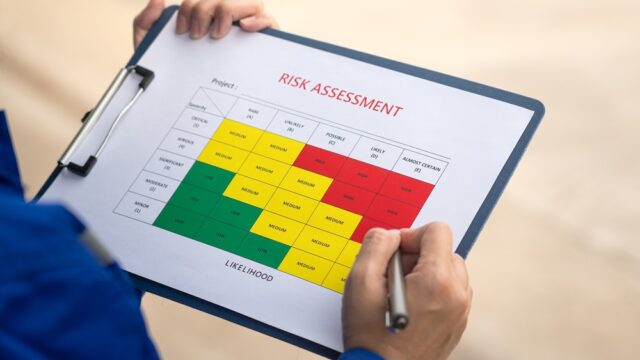 A clipboard with a risk assessment form. Hands hold the clipboard with a pen.