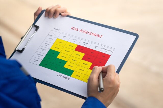 A clipboard with a risk assessment form. Hands hold the clipboard with a pen.