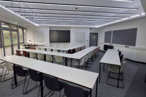 A room with lots of tables and chairs layed out in V shapes.