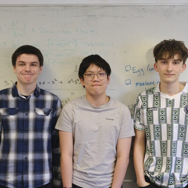 Three students stand side by side in front of a whiteboard.