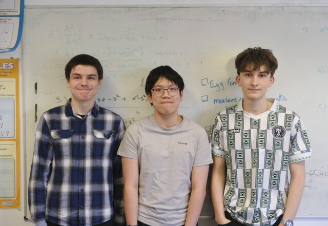 Three students stand side by side in front of a whiteboard.