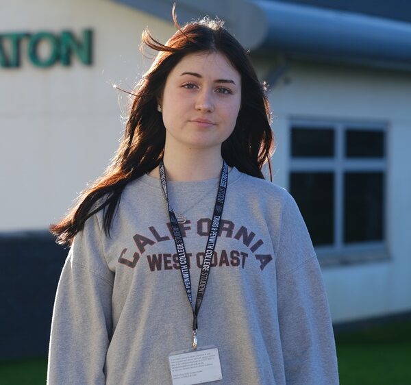 Angie stood outside the Seaton building in a jumper and student lanyard.