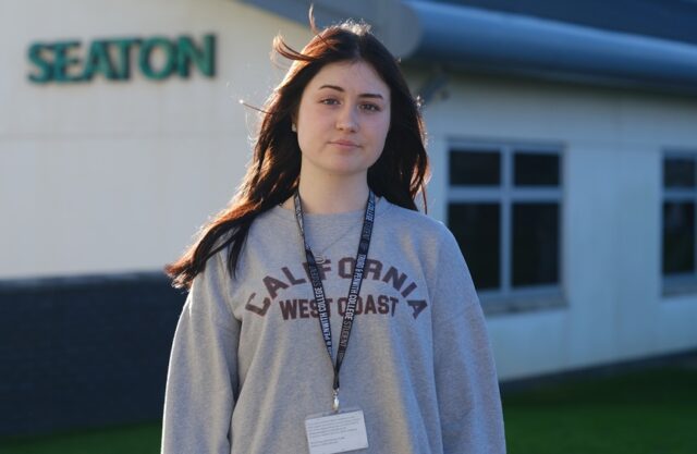 Angie stood outside the Seaton building in a jumper and student lanyard.