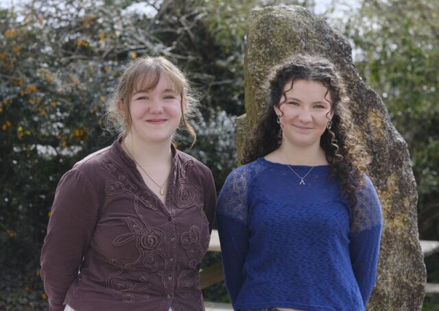Aoife and Ruth stand side by side with a large rock behind them.