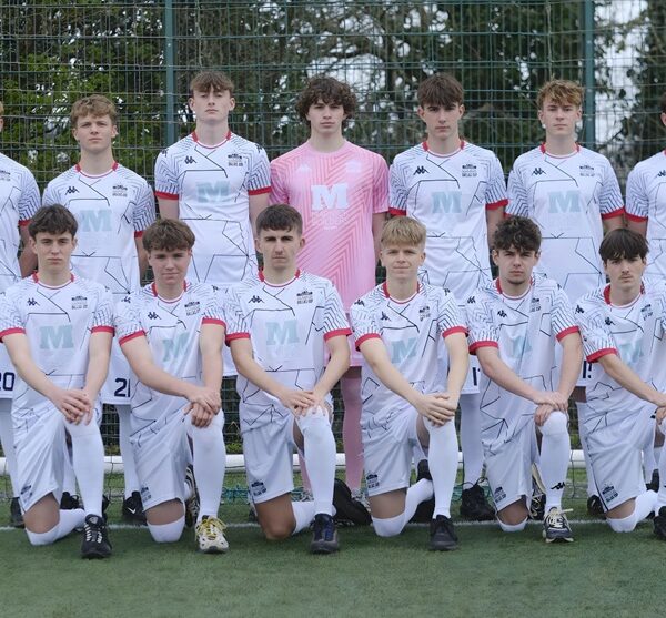 A football squad lined up on a football pitch in white kit.