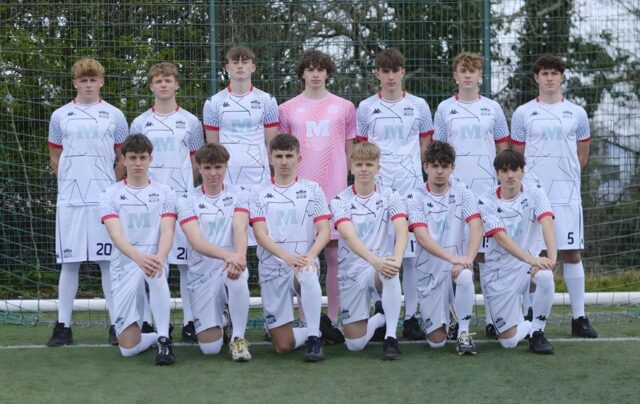 A football squad lined up on a football pitch in white kit.
