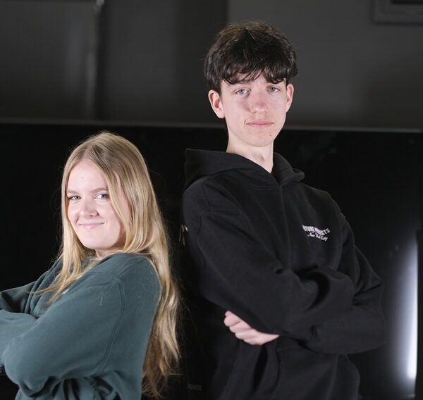 Two students stand back to back with their arms folded across their chests.