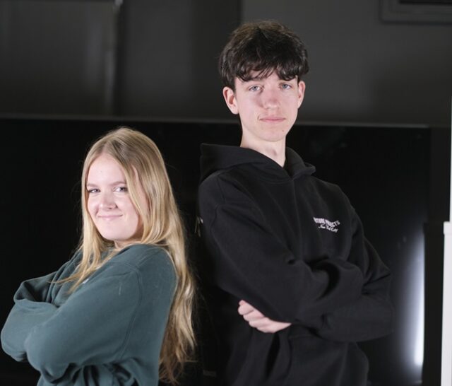 Two students stand back to back with their arms folded across their chests.