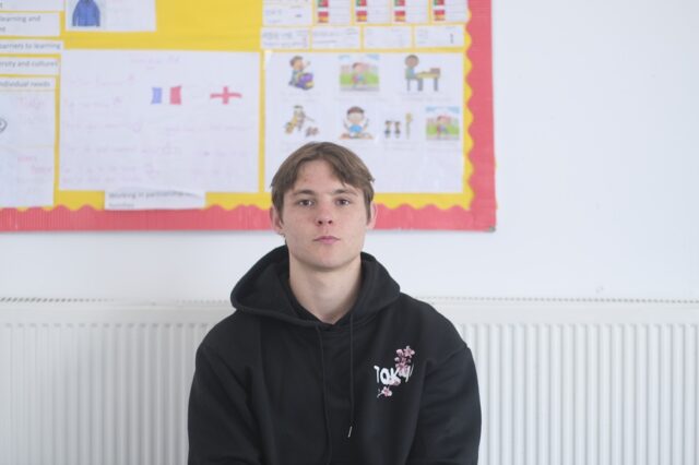 Rowan sat in a classroom wearing a dark hoodie.