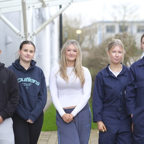 Five students lined up, stood outside. Two are in engineering overalls.