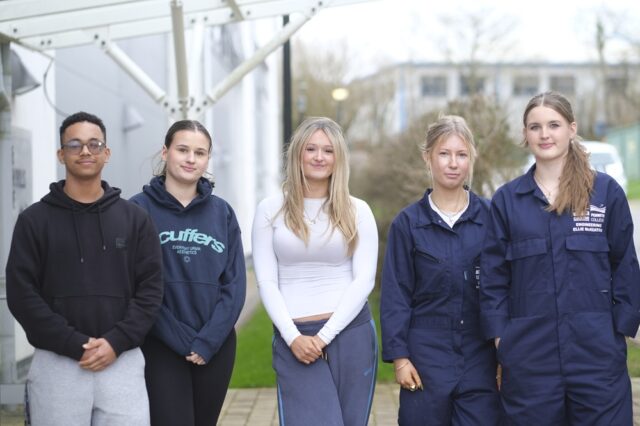 Five students lined up, stood outside. Two are in engineering overalls.