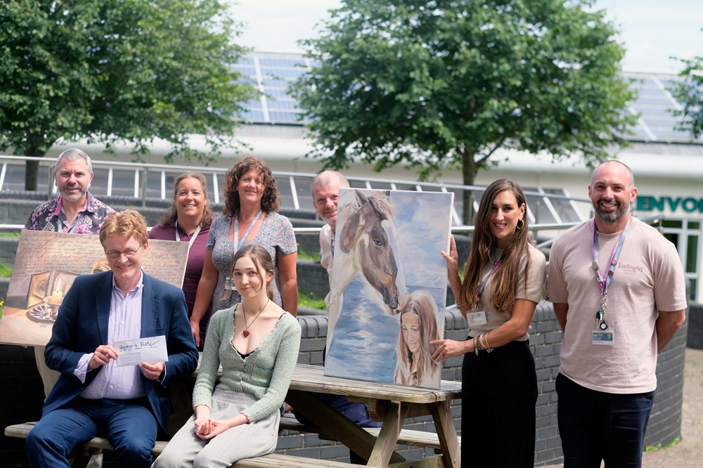 Staff and a student gather outside the college holding a students' artwork.