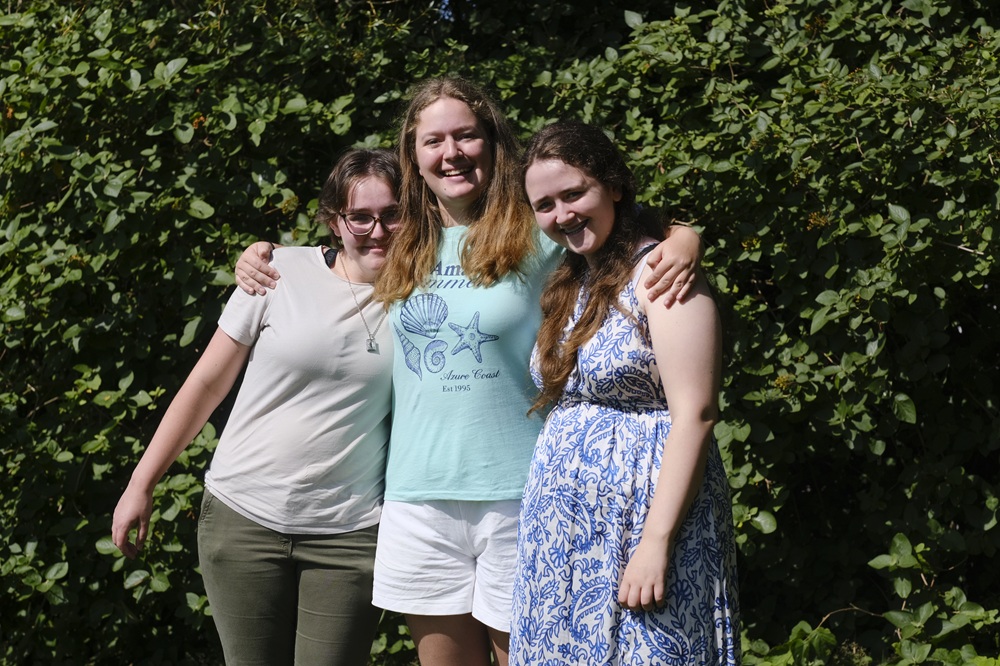 Three girls stand with their arms around each other.