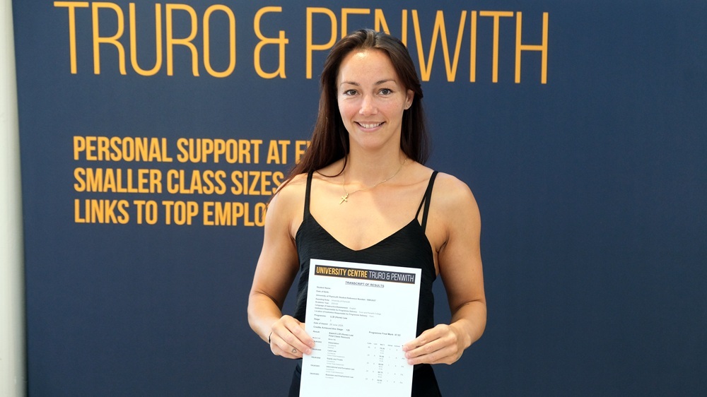 Samantha Elson-Jones holds up her results in front of a banner for the University Centre.