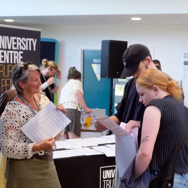 Two students look at their results while a member of staff stands in front of them and smiles.