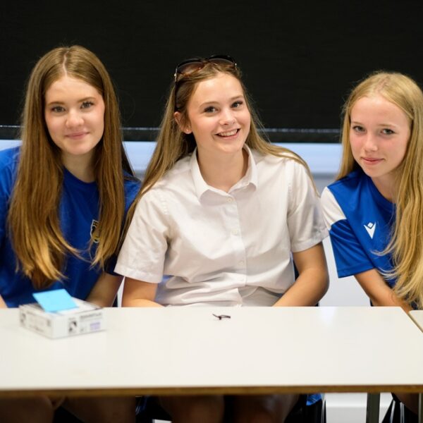 Three girls sit at a classroom table and smile at the camera.