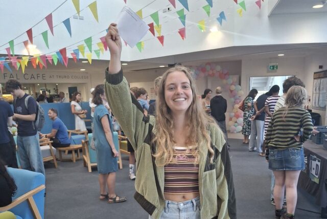 Amelia holding her results up in the air over her head in triumph.