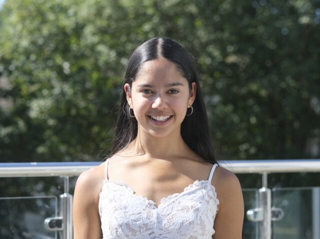 Amelie stood outside at Penwith College. She is wearing a white top and has long dark hair.