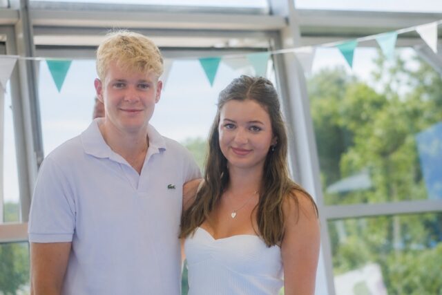 Archie and Cora stood side by side with blue bunting behind them.