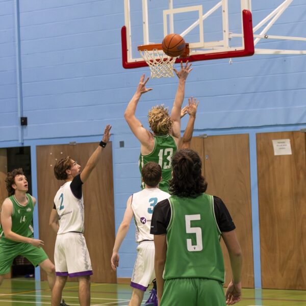 Basketball players jumping towards a basketball hoop.