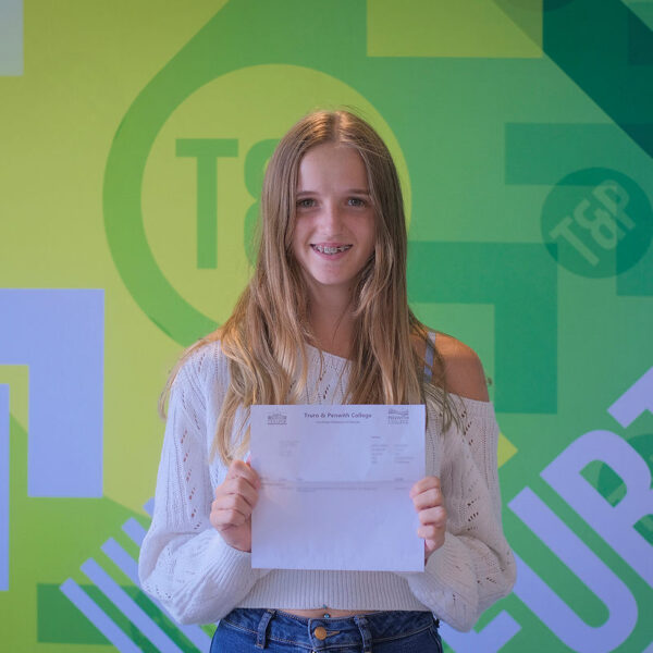 Kara holding up her results in front of a Truro and Penwith College back drop.
