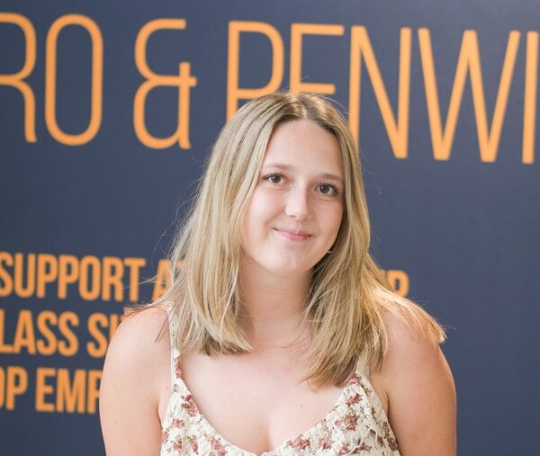 Kenza stood in front of a University Centre banner in a floral dress.