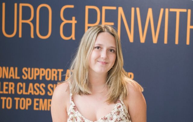 Kenza stood in front of a University Centre banner in a floral dress.