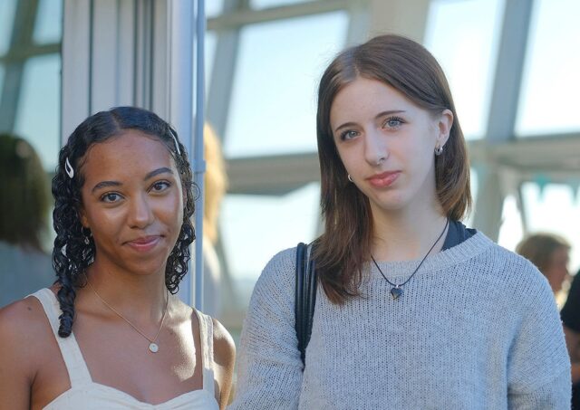 Millie and Mareme stood in front of a large window smiling at the camera.
