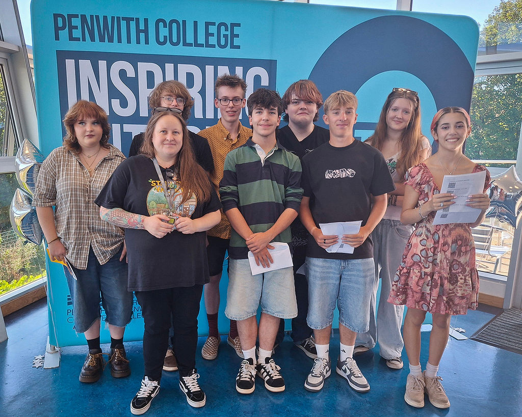 A group of students with their tutor standing in front of a Penwith College banner holding their results.