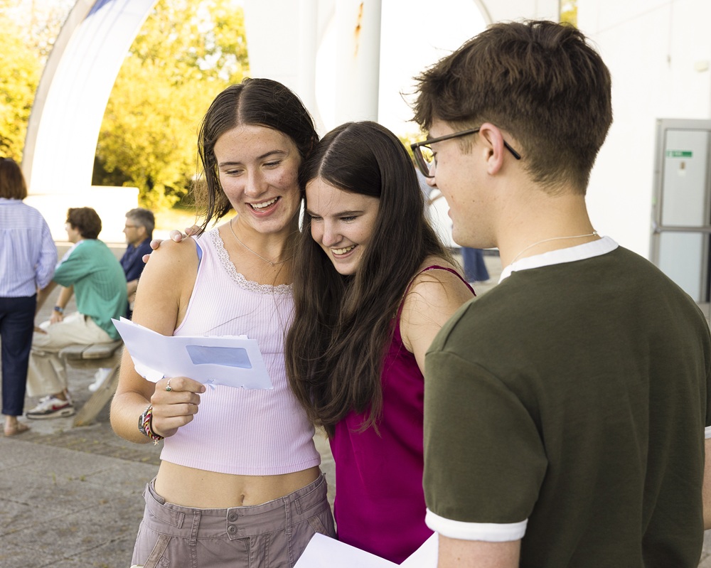 Friends with their arms around each other looking at their results. They have big smiles.