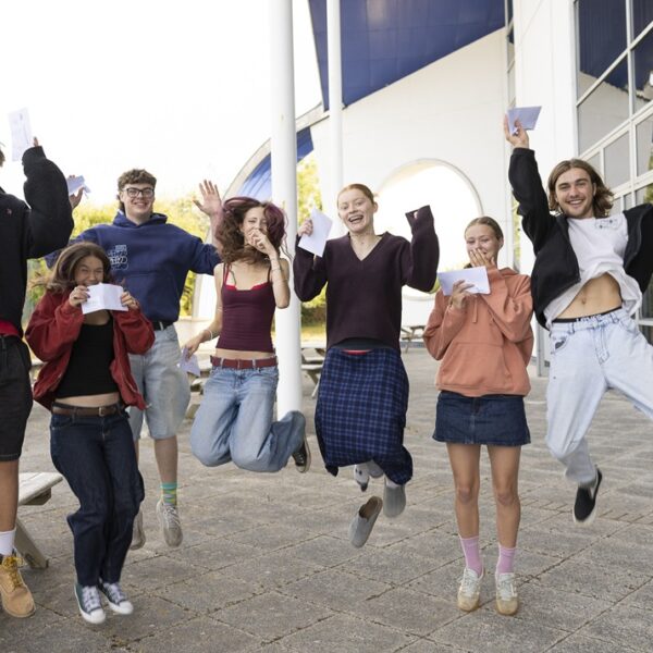 A group of students leaping into the air for joy, holding envelopes in their hands.
