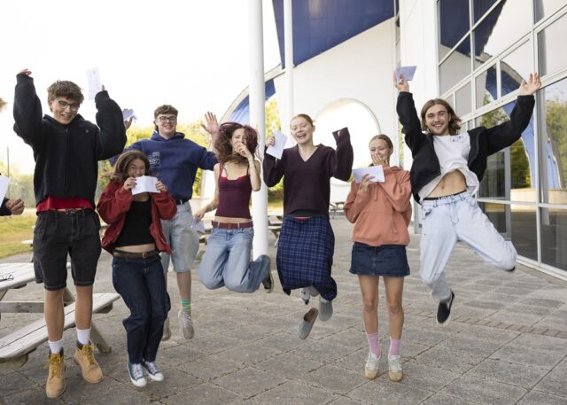 A group of students leaping into the air for joy, holding envelopes in their hands.