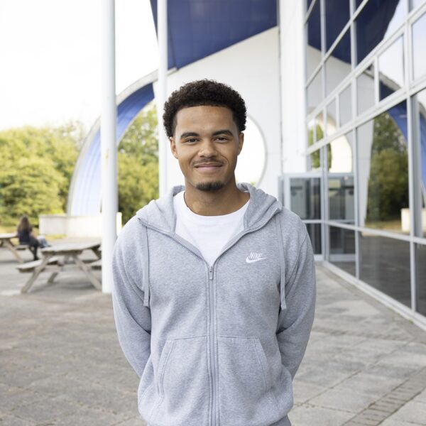 Rhys stood outside at Truro college wearing a grey hoodie. His hands behind his back.