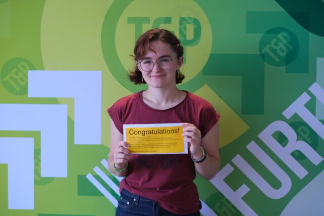 Olivia stands smiling, holding exam results letter