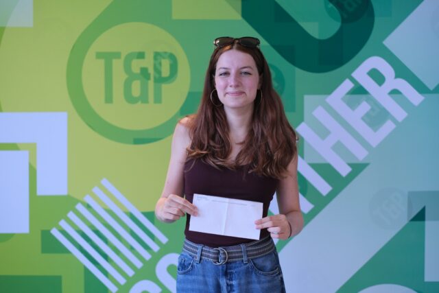 Katie smiles as she hold her exam results letter