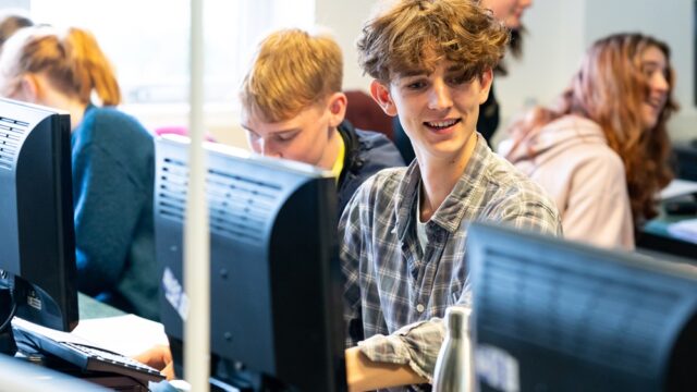 Students sit at computers and smile.
