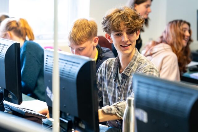 Students sit at computers and smile.