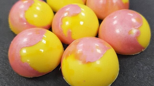 A close-up of paink and yellow sweets on a dark grey slate.