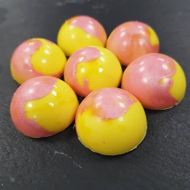 A close-up of paink and yellow sweets on a dark grey slate.
