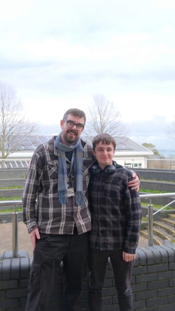 (R-L) Lecturer Joe Sandles stood with his arm around Joe. Both stood outside smiling.