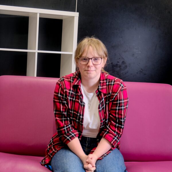 Katie sat on pink sofa, smiling with hands clasped.