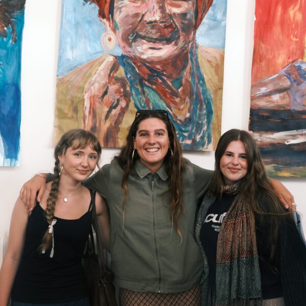three students stood smilining in front of paintings