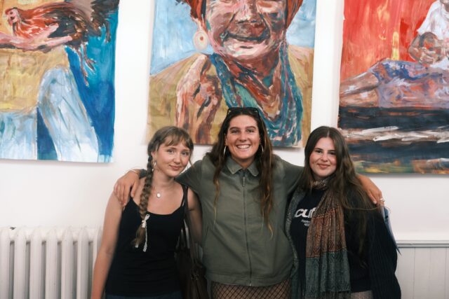 three students stood smilining in front of paintings
