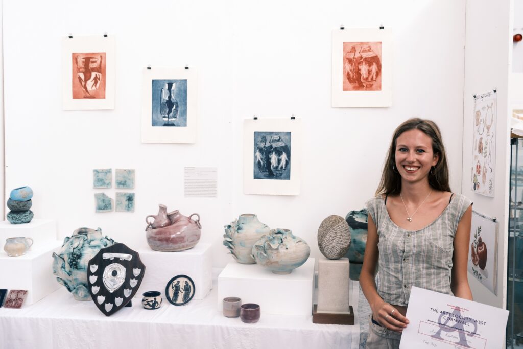 Amelie stood smiling, holding a certificate in front of a display of her work.