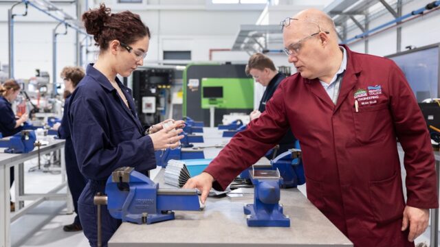 A tutor and a student look at pieces of metal within a workshop.