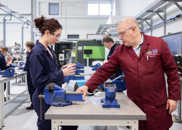 A tutor and a student look at pieces of metal within a workshop.