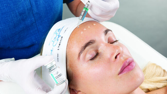 A client is having hyaluronic glide serum applied to their forehead by an unknown professional.