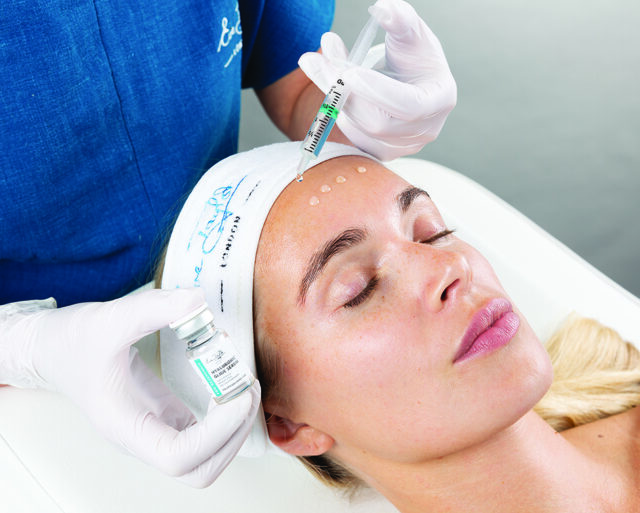 A client is having hyaluronic glide serum applied to their forehead by an unknown professional.