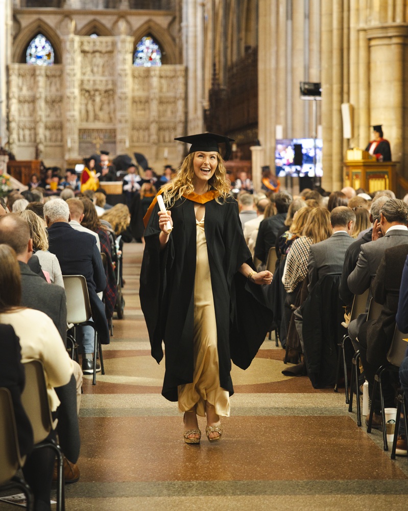 A graduate walking down the centre aisle of Truro cathedral with a scroll in their hand.
