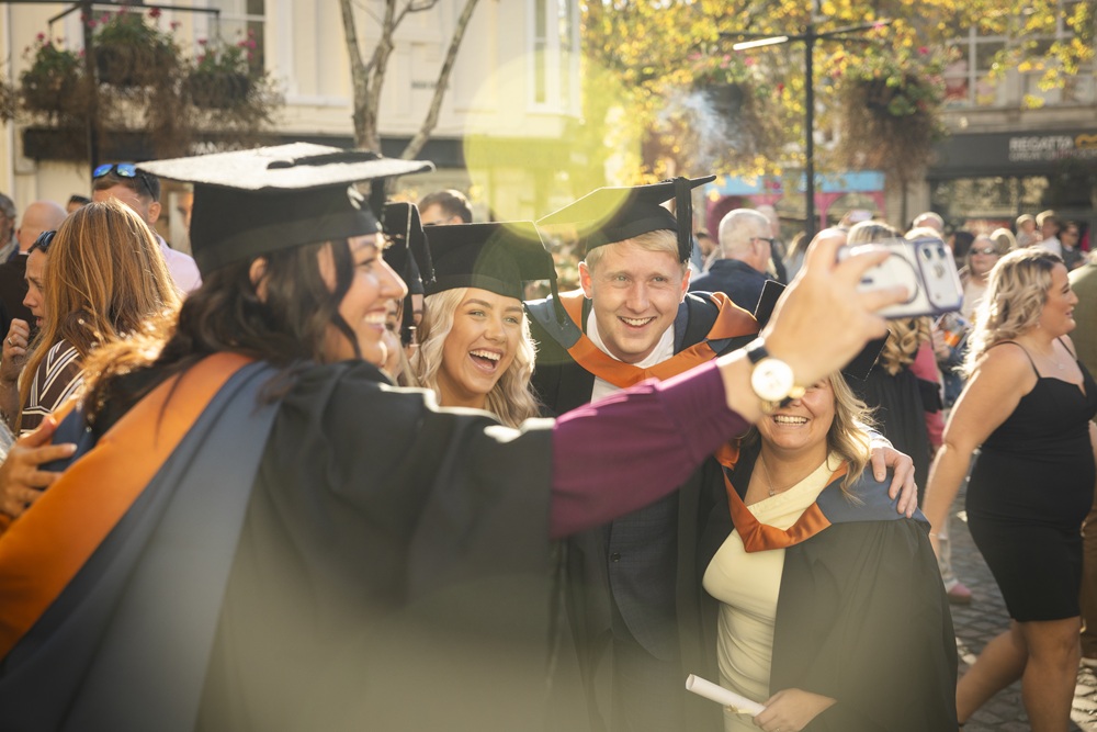 A group of graduates taking a selfie outside Truro cathedral in the sun.